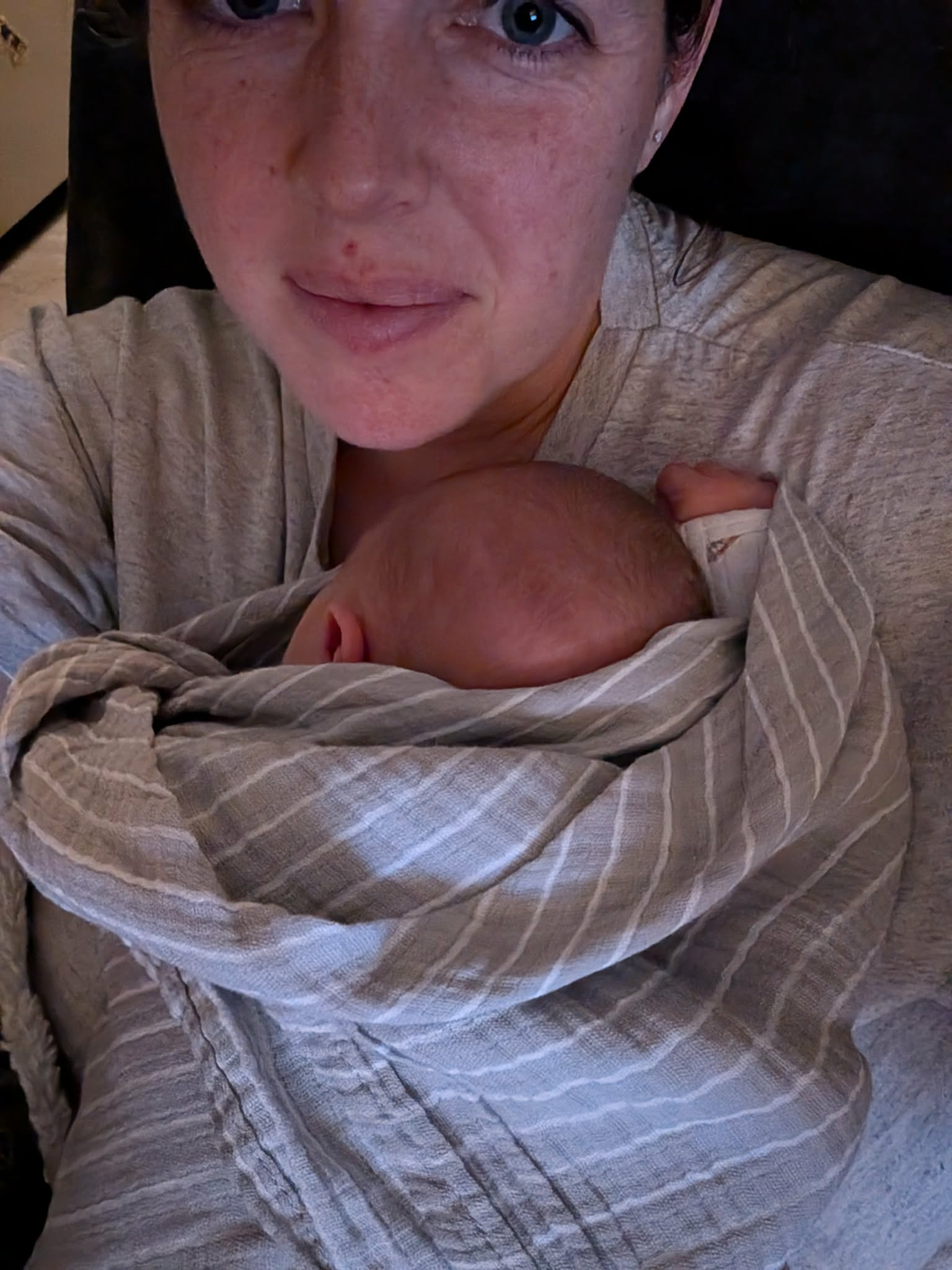 A mother holding her sleeping newborn against her chest in a striped wrap